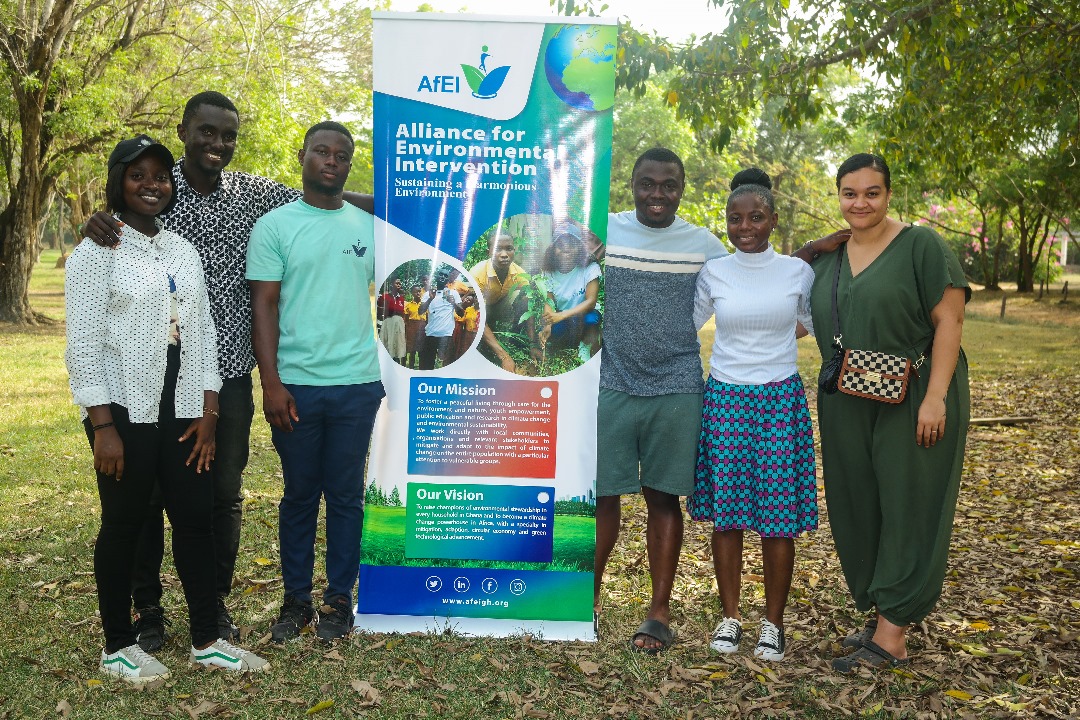 Six people standing together outdoors beside an Alliance for Environmental Intervention banner