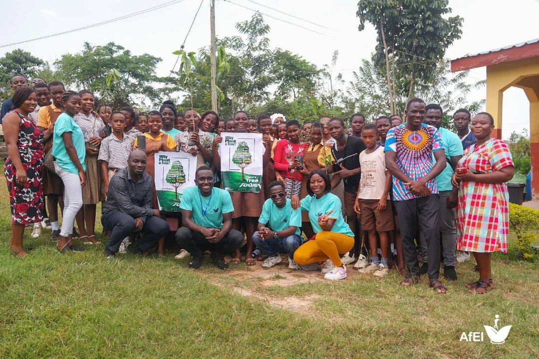 Students, teachers and community members posing outdoors, some holding tree-planting posters
