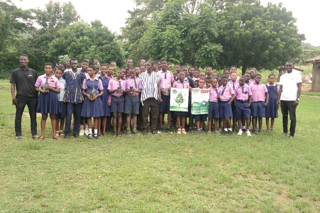 Students in pink school uniform standing together on a lawn, two people holding posters, image 2 of 12